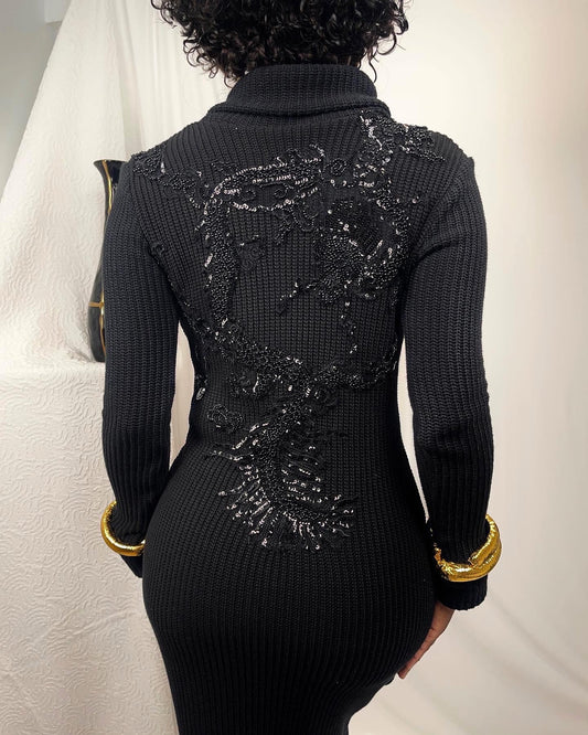 Back view of this chunky cotton sweater dress showcases a black beaded dragon. This stretch knit is paired with gold hue faux bangles at the end of the sleeve hem and a high fold over collar. 