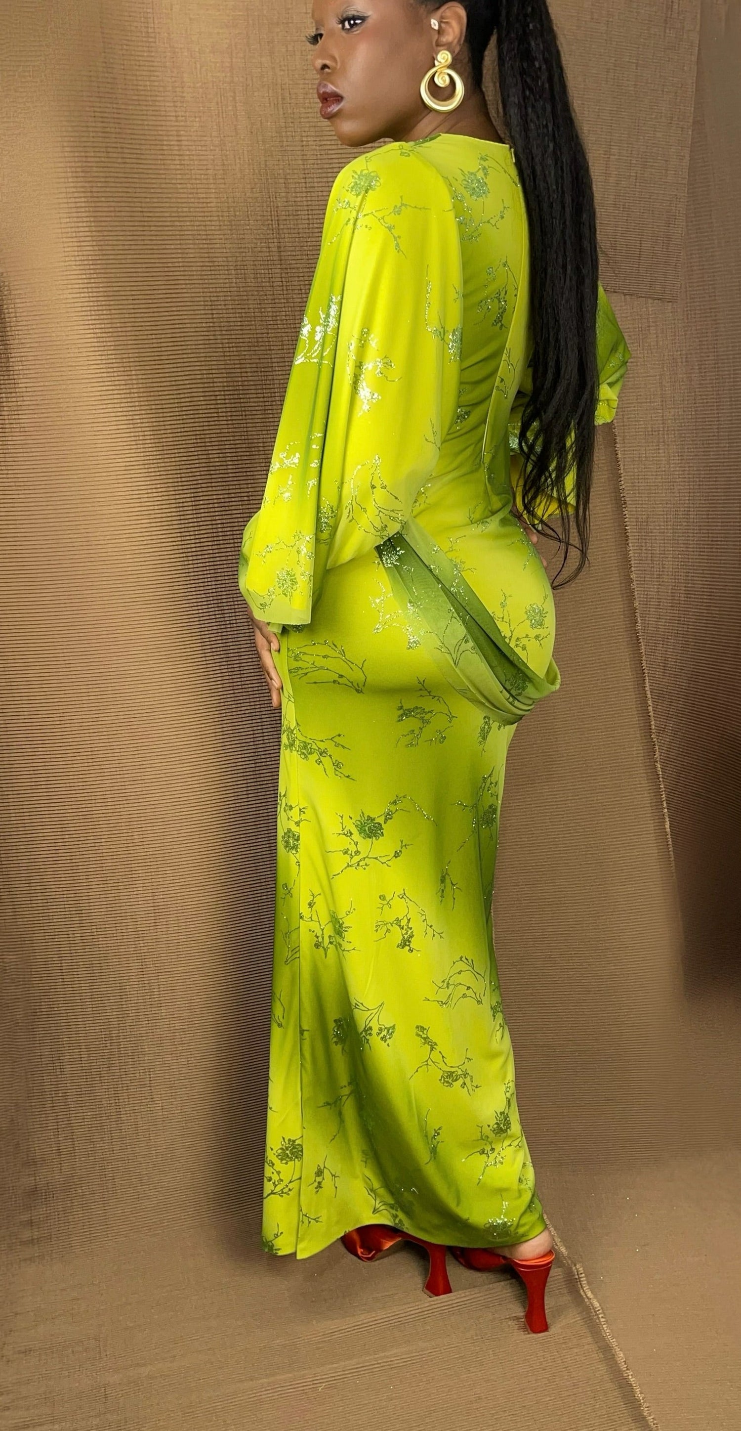 Back view of our ombre green and yellow modest dress. Dress details glitter floral pattern all over, and a drape sash across one shoulder. The sleeves feature a asymmetrical style while staying light and flowy.  