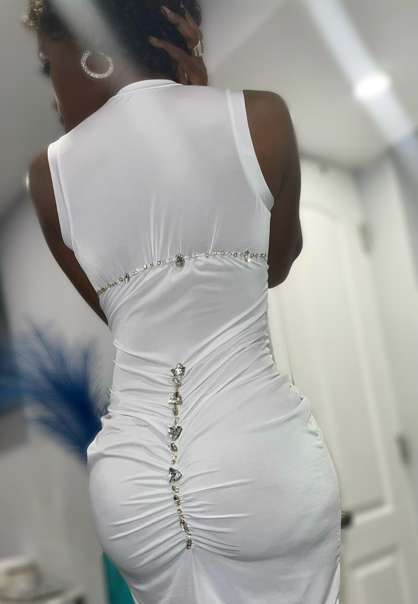 Back view of a sleeve less tank style white dress. Dress is both cool and elevated with both small and large rhinestones placed across the back shoulder length. The rhinestones are then placed down the mid center back of the dress. The garment will stretchy and form fitting to the body.