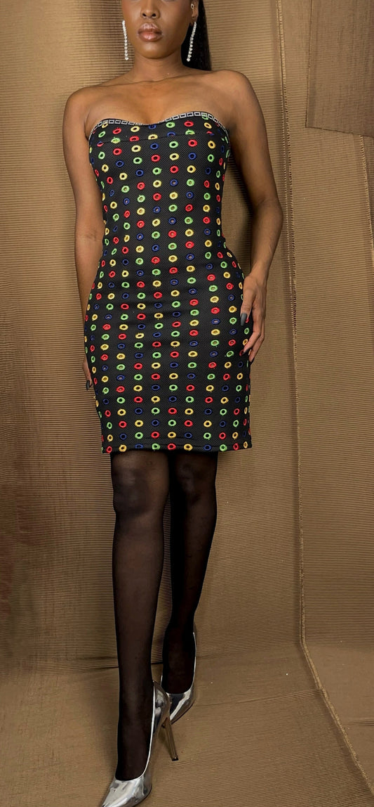 Front view of our tube cut style black multi color embroidered dress. Dress features embroidered small circles in a ray of colors. The colors are yellow, navy blue, red, and green. The bust showcase hand sewn black and silver square rhinestone trim and is above knee in length.