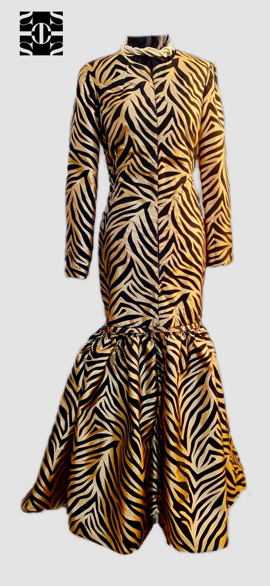 Gold Taffeta black velvet tiger stripe dress. The fabric has a soft gold sheen all around with black stripes patterned all over. The dress is a more tailored fit with a flared out bottom. Dress can be worn as a mini and the bottom can be used as a cape. There is a center front zipper, long sleeves and a high neckline.
