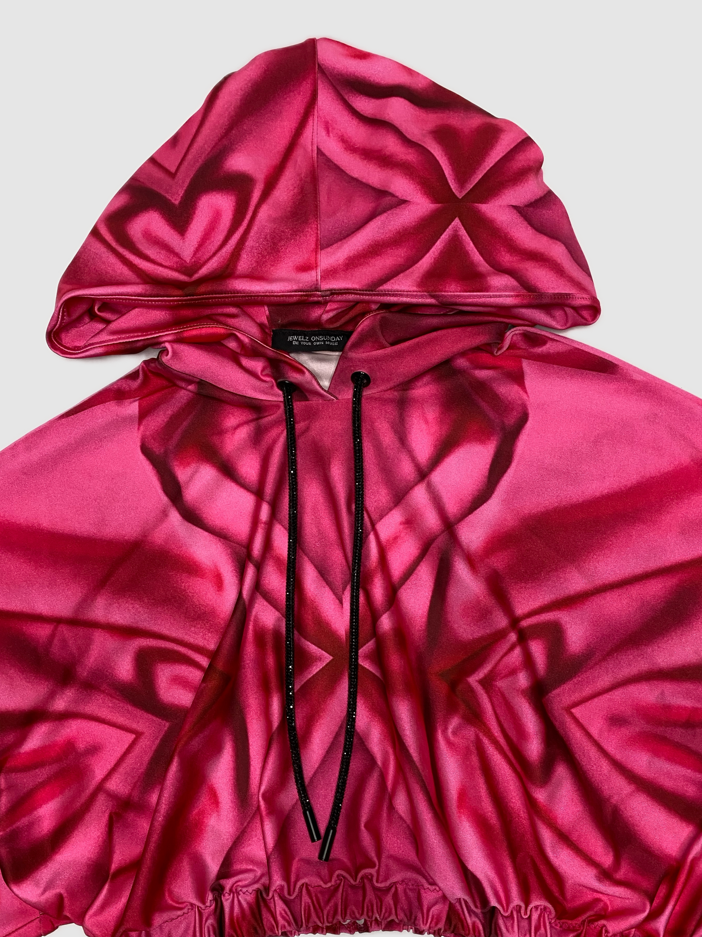 Our custom print consist of hearts, swirls and x's in a range of pink shades. The print was curated on a Lycra soft sheen fabric. Each hoodie pattern is unique. This hand crafted loose fit Kimono sleeve cropped hoodie, is fitted with an elastic waistband. A black sparkling crystal drawstring is spun around the hood. The functionally designed hoodie allows the wearer to pull their hair through the stretchy band at the back of the hood.