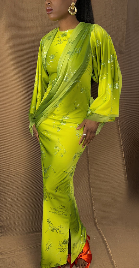 Front view of our ombre green and yellow goddess dress. Dress features a drape pleated sash across the shoulder while draping across the body. There is a small slit on one side of the garment and the dress reaches ankle length. Modest summer dress with a green floral glitter pattern across the body.