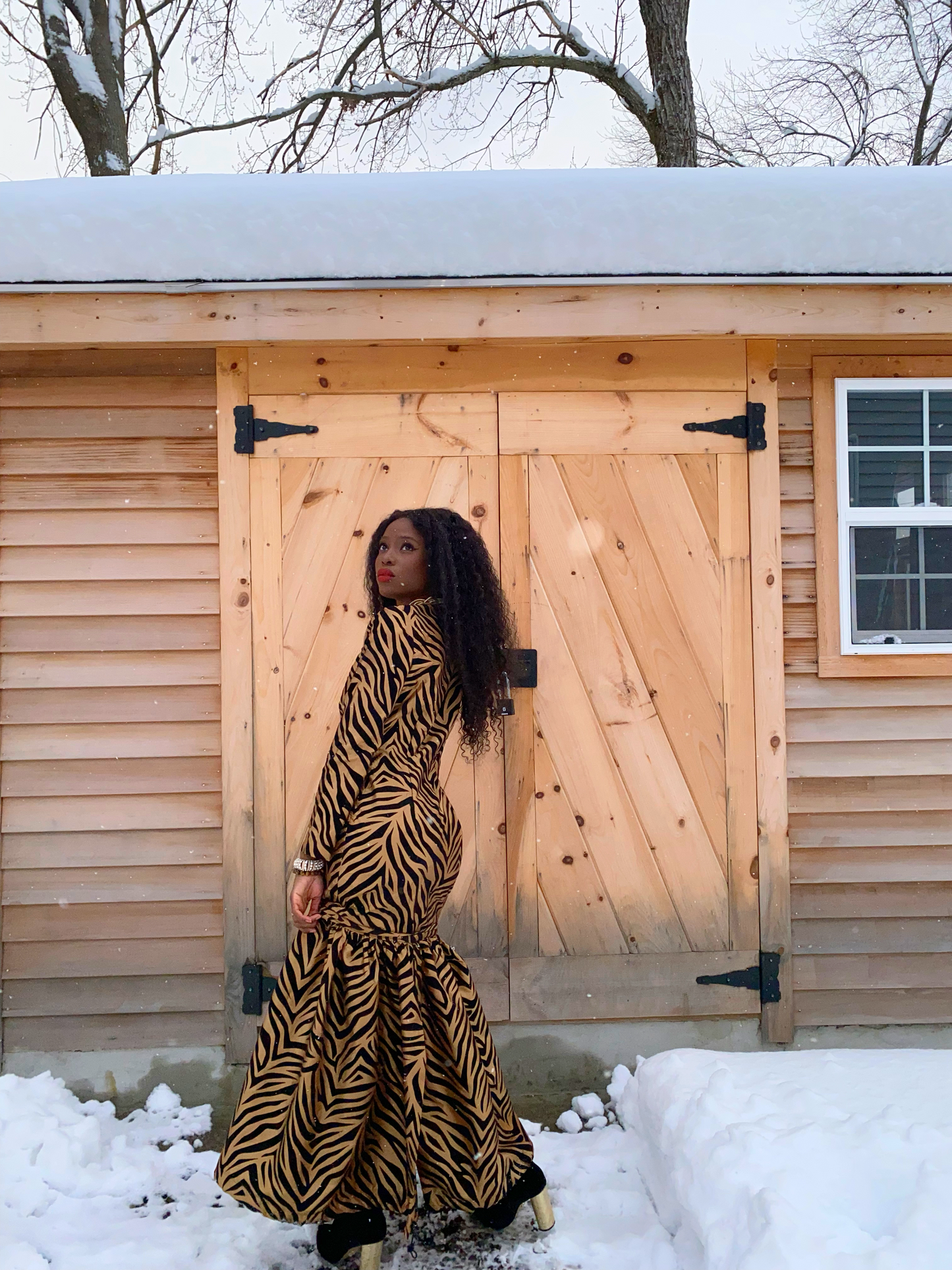 image depicts women wearing a tailored gown. The fabric has a gold soft sheen to it. The fabric is made out of taffeta, and their are black velvet tiger stripes patterned all over the dress. The dress also features a flared bottom that can be detached.