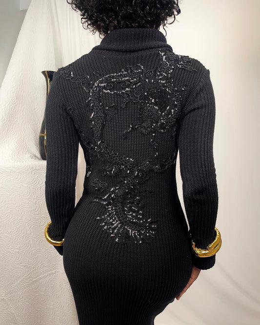 Back view of this chunky cotton sweater dress showcases a black beaded dragon. This stretch knit is paired with gold hue faux bangles at the end of the sleeve hem and a high fold over collar.
