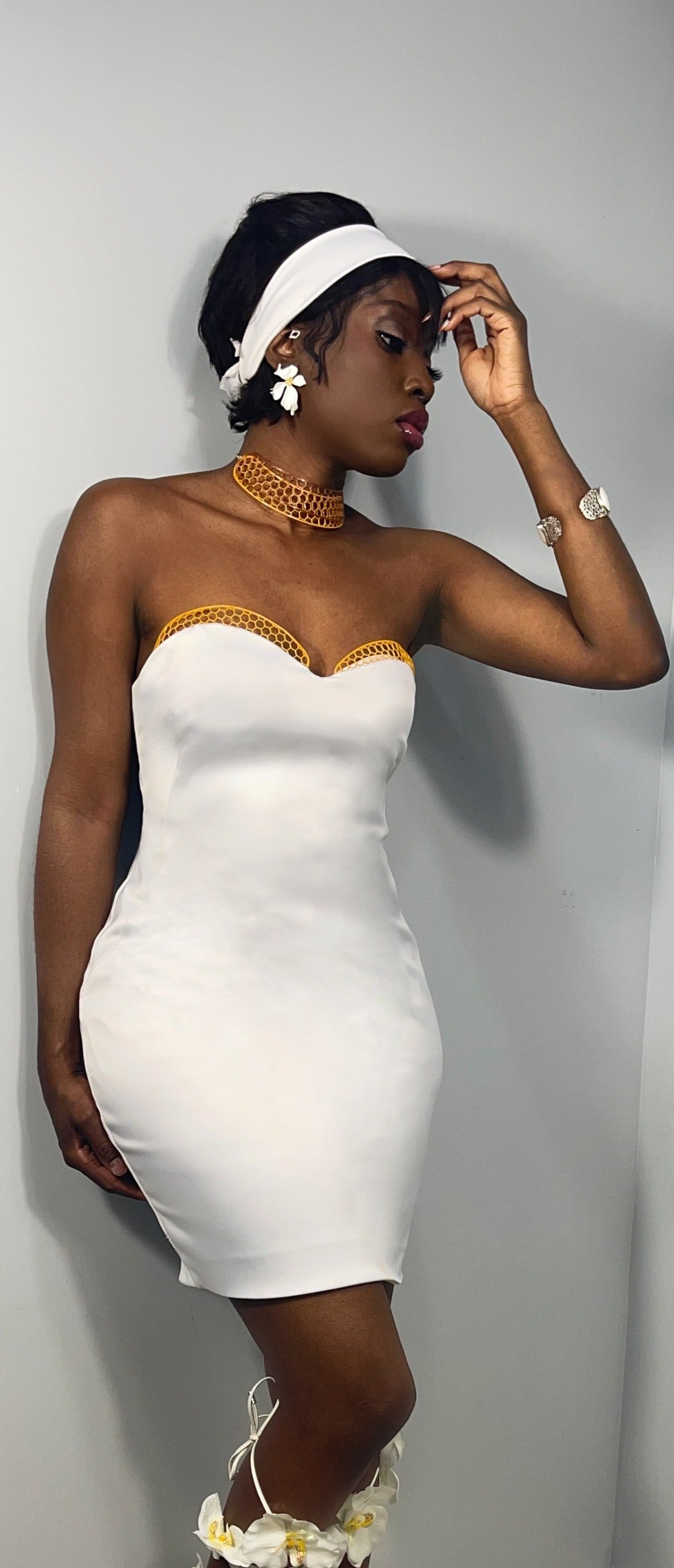 Model posing in a above knee white dress with 3d printed honeycomb trim across the bust neckline of the dress. Garment is strapless sweet heart neckline with a slim fit design style. 