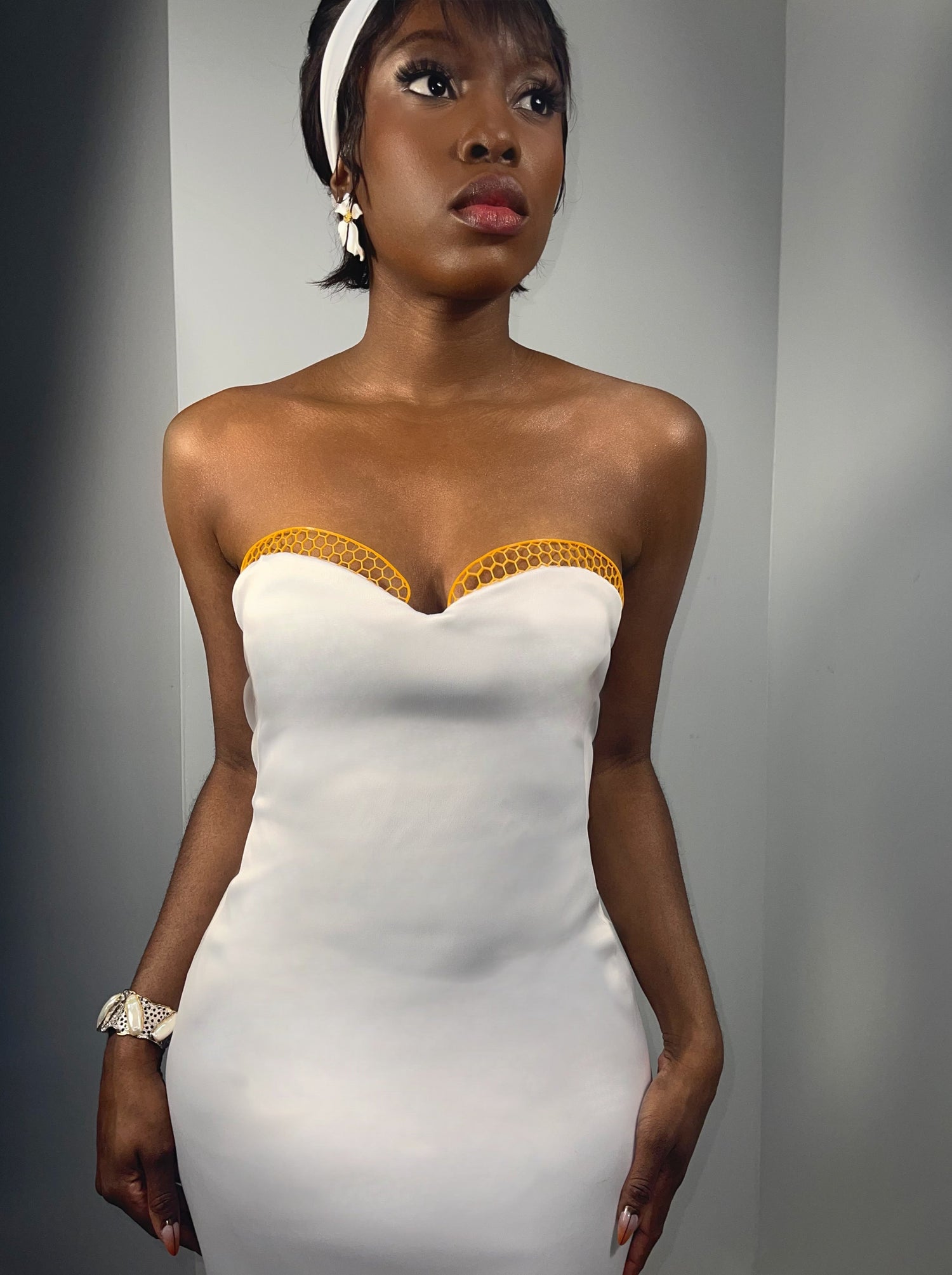 Front view of model posing in a above knee white dress. Strapless dress features a sweetheart neckline and 3d printed honeycomb trims around the bust in contrasting color. Slim fit style dress with tailored French darts. Silk dress inspired by the queen honey bee. 