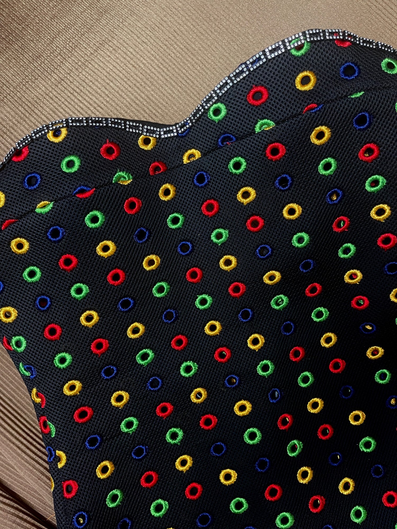 Detail view of front bodice dress. This black multi color dress features embroidered small circles in different colors, and a rectangle black and rhinestone trim around the top bustline. 