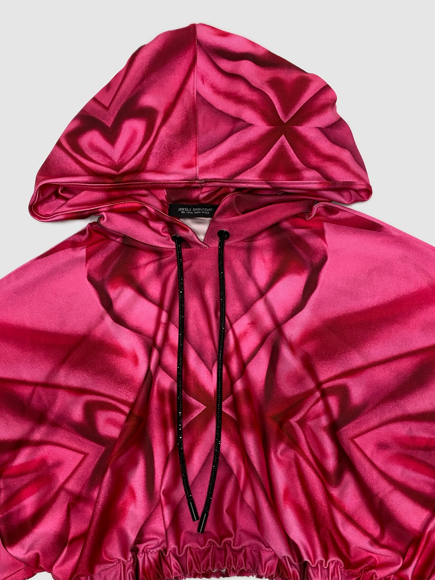 Our custom print consist of hearts, swirls and x's in a range of pink shades. The print was curated on a Lycra soft sheen fabric. Each hoodie pattern is unique. This hand crafted loose fit Kimono sleeve cropped hoodie, is fitted with an elastic waistband. A black sparkling crystal drawstring is spun around the hood. The functionally designed hoodie allows the wearer to pull their hair through the stretchy band at the back of the hood. 