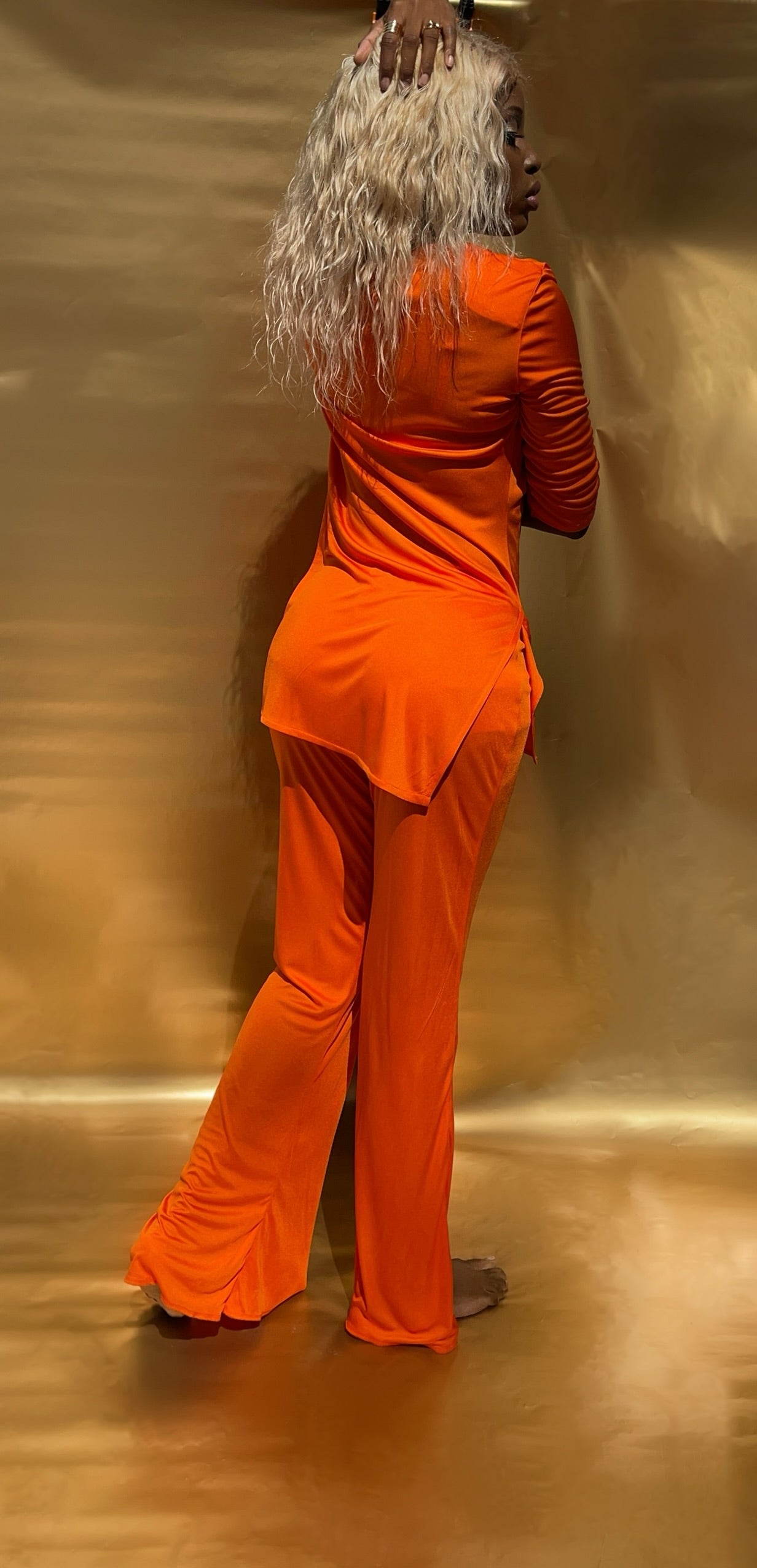 Back view of floor length wide leg flowy pants. Pants is made out of a soft delicate viscose fabric in a warm orange color.