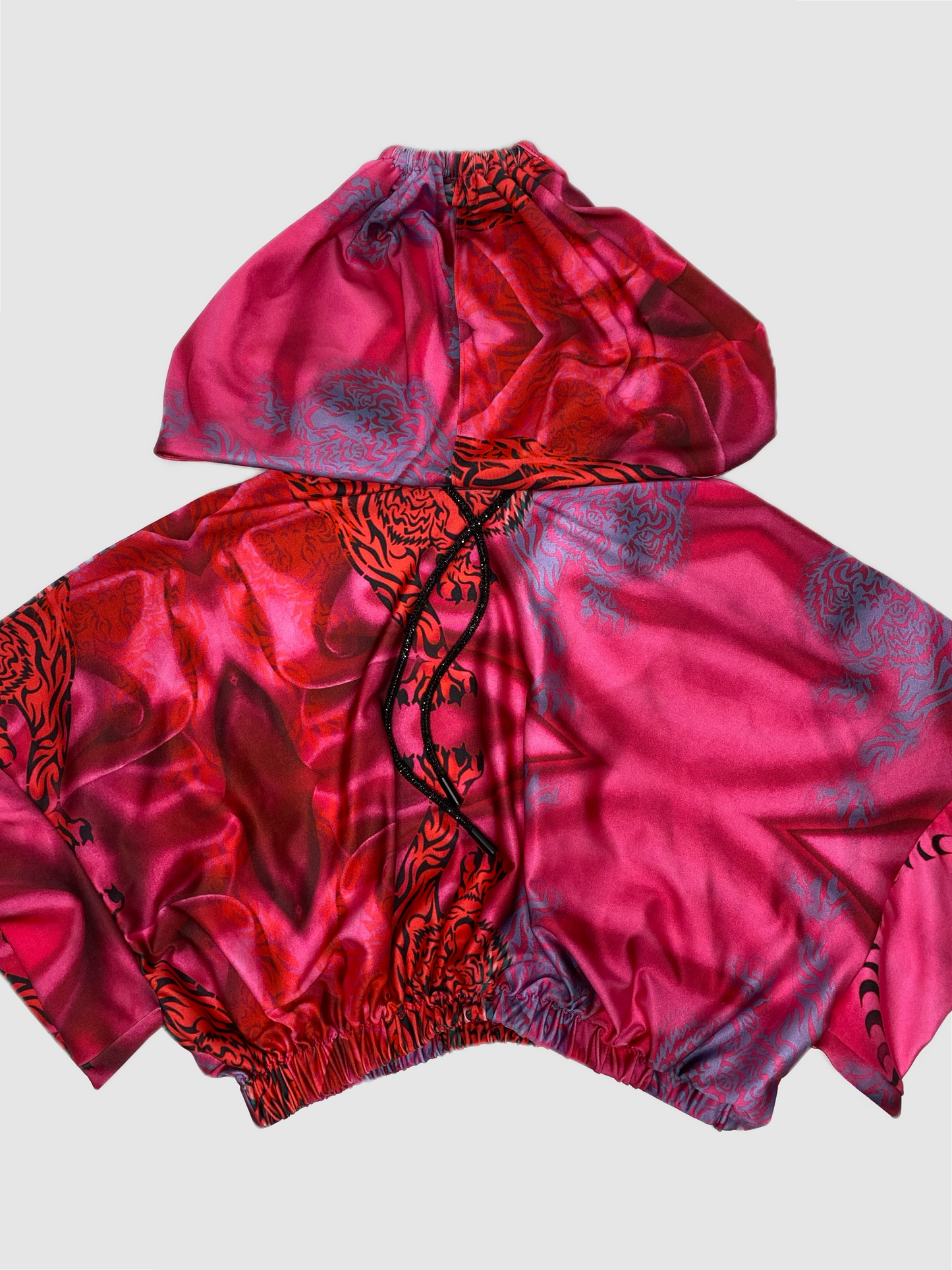 Our custom print consist of repeated tigers, and geometric shapes. The print was curated on a Lycra soft sheen fabric. Each hoodie pattern is unique. This hand crafted loose fit Kimono sleeve cropped hoodie, is fitted with an elastic waistband. A black sparkling crystal drawstring is spun around the hood. The functionally designed hoodie allows the wearer to pull their hair through the stretchy band at the back of the hood. The print features a range of pink shades from light pink to fuchsia. 