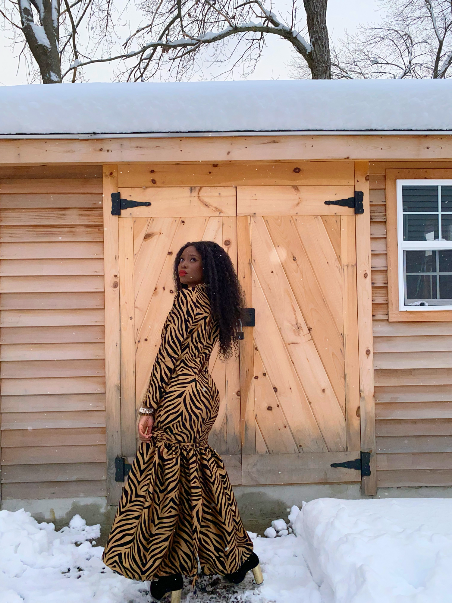 image depicts women wearing a tailored gown. The fabric has a gold soft sheen to it. The fabric is made out of taffeta, and their are black velvet tiger stripes patterned all over the dress. The dress also features a flared bottom that can be detached. 